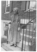 SA0053 - Identified on reverse. Tillie Schnell is standing on the steps of an unknown building holding a basket.